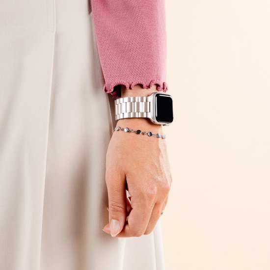 Een pols met een zilverkleurig stalen bandje om een smartwatch. Een roze trui en beige rok worden gedragen.