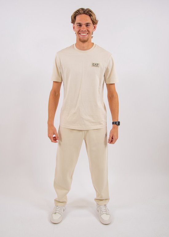 Man in een lichtbeige EA7 T-shirt en bijpassende joggingbroek met fijne ribbels.