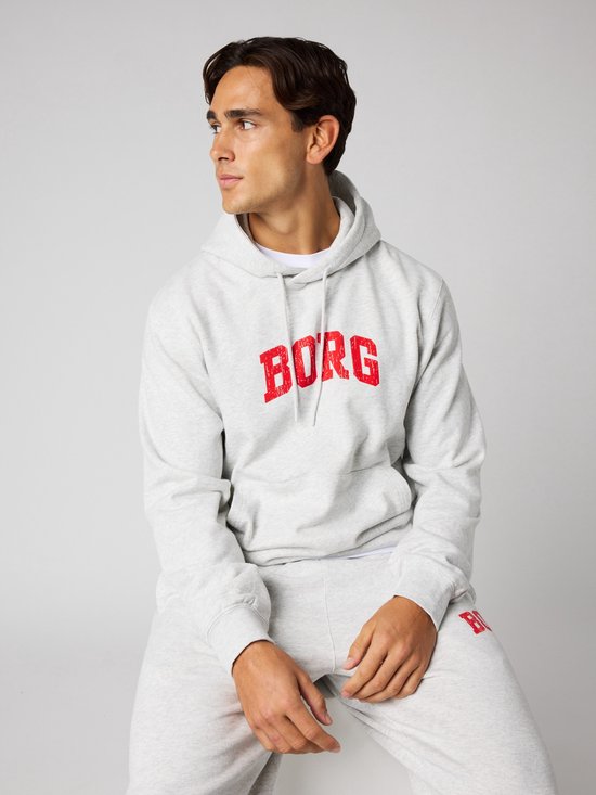 Man zittend in een lichtgrijze hoodie met rode 'BORG' letters op de borst.