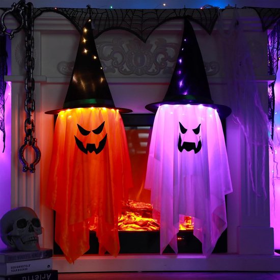 Twee verlichte spookdecoraties met heksenhoeden voor een open haard. Eén is oranje, de andere paars, met gloeiende gezichten.