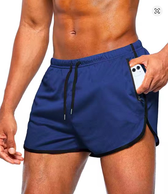 Man in blauwe sportbroek met split aan de zijkant en een telefoon in een zak.