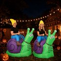 Een man en een vrouw in opblaasbare slakkenkostuums zitten buiten bij nacht, met Halloween-decoraties.