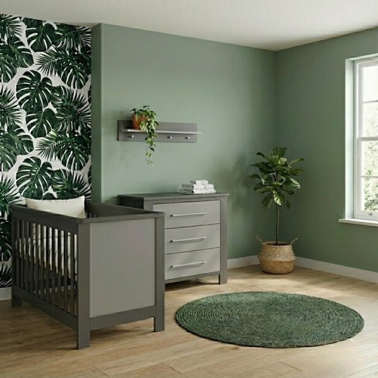 Grijze babykamer met commode, babybed, ronde groene mat en groene muur met planten.