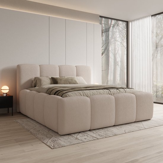Lit double en tissu beige avec tête de lit rembourrée et base enveloppante de forme carrée. Drappé de couvertures et coussins taupe.