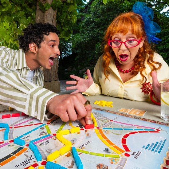 Twee spelers met verbaasde gezichten spelen een bordspel met een kaart van Europa en gekleurde treintjes.
