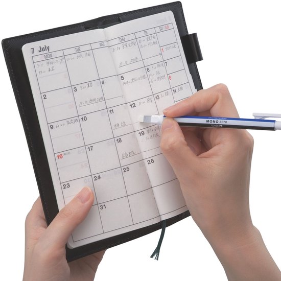 Handen gebruiken een Tombow Mono zero pen om een agenda te wissen, met een blauwe en zwarte pen.