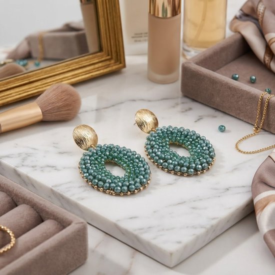 Grote, ovale turquoise groene oorbellen met gouden details, opgemaakt op een marmeren oppervlak.