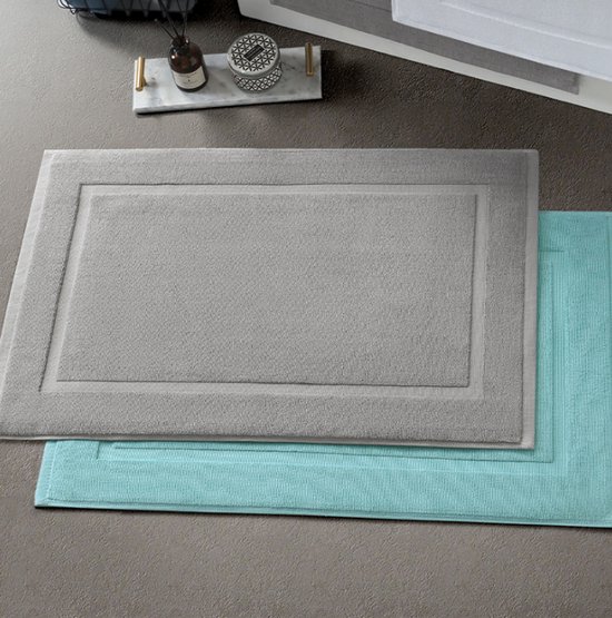 Een grijze badmat ligt bovenop een turquoise badmat.