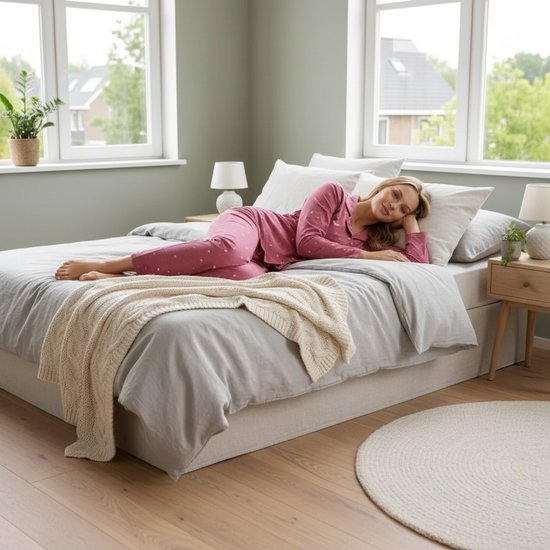 Vrouw liggend op een bed in roze pyjama met hartjesprint.