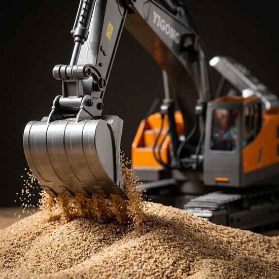 Close-up van de metalen bak van een grijze en oranje RC graafmachine die zand schept.