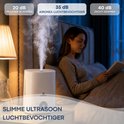 Vrouw leest een boek in bed, naast een ultrasone Aironex luchtbevochtiger die stoom produceert.