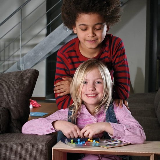 Jongen met afro-kapsel en meisje met blond haar spelen IQ Fit spel aan een tafel. Het meisje heeft de stukken in haar handen.