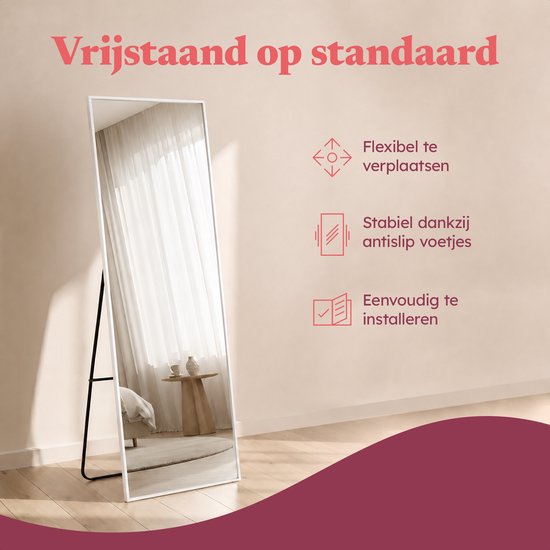 Een staande spiegel met witte lijst staat op een zwart metalen onderstel. Tekst: Vrijstaand op standaard.