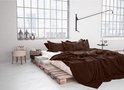 Een slaapkamer met een bed opgestapelde pallets, gedrapeerd met bruine dekens en kussens.