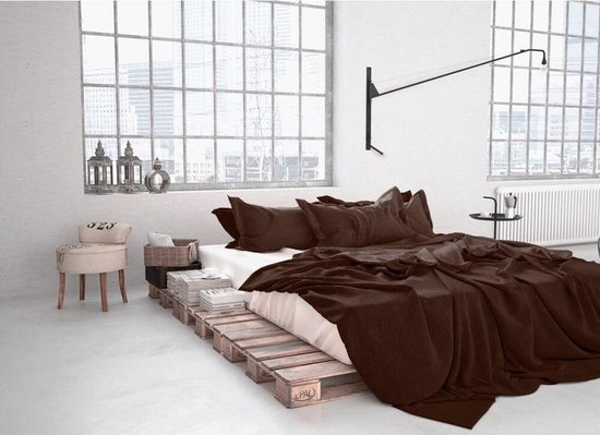 Een slaapkamer met een bed opgestapelde pallets, gedrapeerd met bruine dekens en kussens.