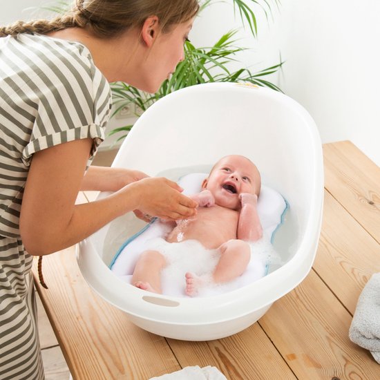 Moeder helpt baby in bad op wit matrasje met lichtblauwe rand.