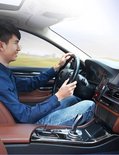 Man in blauw shirt en spijkerbroek rijdt auto met telefoonhouder op dashboard.