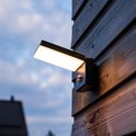 Moderne zwarte wandlamp met sensor, schijnt warm licht op houten schutting.