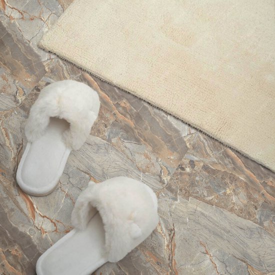 Witte pluizige slippers op een grijze marmerlook vloer naast een beige kleed.