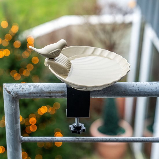 Olijfgroen vogelbadje met vogeldecoratie, bevestigd aan een reling op een balkon.