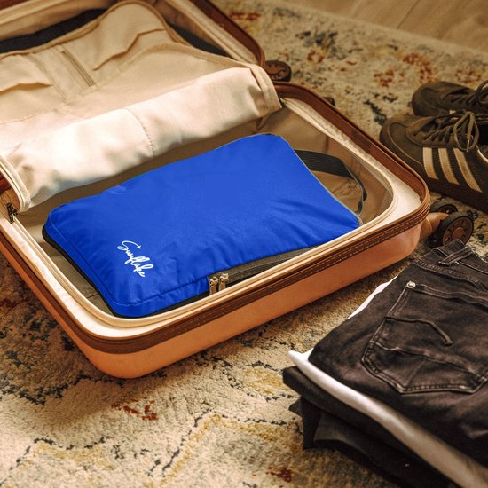 Een blauwe Sunflake packing cube met logo in een koffer, naast kleding en schoenen.