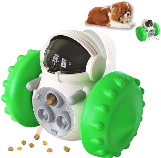Wit en grijs robotvoederspeelgoed met grote groene wielen, dat brokjes verspreidt. Kleine hond ligt op de achtergrond.