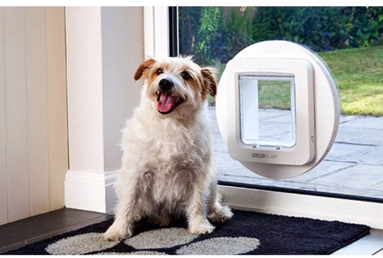 Een witte hond zit voor een glazen deur met een rond wit SureFlap huisdierluik.