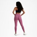 Vrouw met handen in de zij, draagt roze sportlegging en zwarte sportbeha.