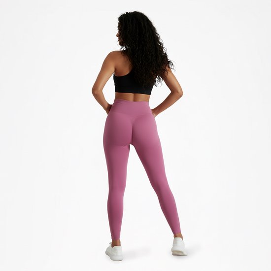 Vrouw met handen in de zij, draagt roze sportlegging en zwarte sportbeha.