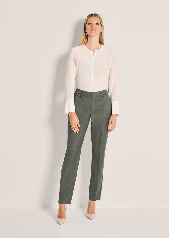 Model in grijze wollen broek met persvouw en crèmekleurig overhemd met lange mouwen.