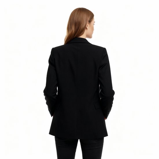 Model met de rug naar de kijker, draagt een zwarte oversized blazer met de revers naar buiten. Zwarte broek.