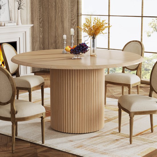 Table à dîner ronde avec plateau en bois à chevrons et pied cannelé, photographiée dans un salon avec cheminée.