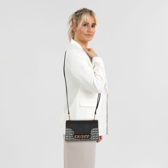 Model draagt een zwarte DKNY crossbody tas met logo-print en goudkleurige letters.