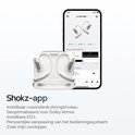 Wit Shokz OpenFit Pro oordopjes in een oplaadcase, naast een smartphone met de Shokz app.