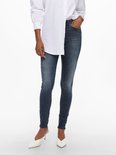 Dames in een donkerblauwe skinny jeans met lichte wassing. Witte blouse en witte puntige muiltjes.