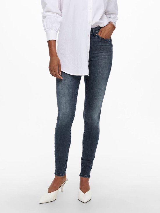 Dames in een donkerblauwe skinny jeans met lichte wassing. Witte blouse en witte puntige muiltjes.