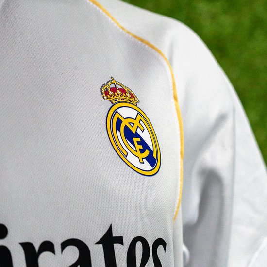 Detail van het Real Madrid clublogo op een wit voetbalshirt met oranje stiksels.