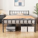Cadre de lit en métal noir avec couette à rayures, couverture et valises de rangement sous le lit, avec une plante sur le côté.