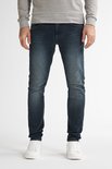 Man met donkerblauwe slim fit jeans, licht vervaagd aan de voorkant, met witte sneakers.