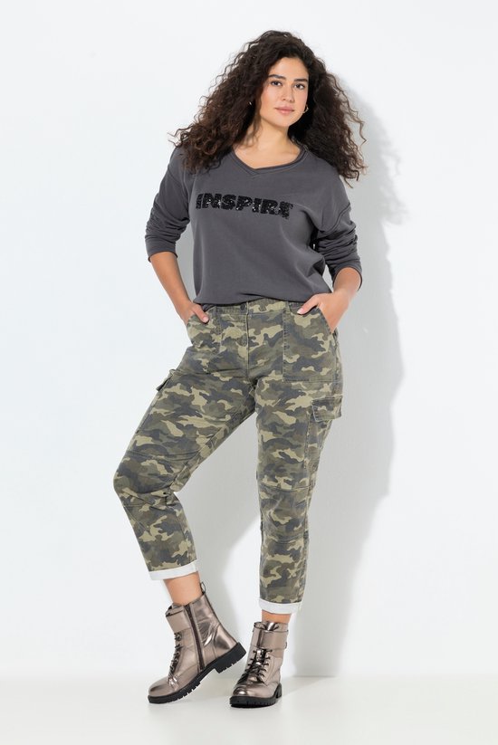 Model draagt een grijze sweater met 'INSPIRE' opdruk en een camouflage broek met opgestikte zakken en opgerolde zoom.