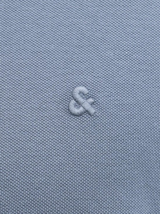Detail van een geborduurd '&'-symbool op een blauw poloshirt.