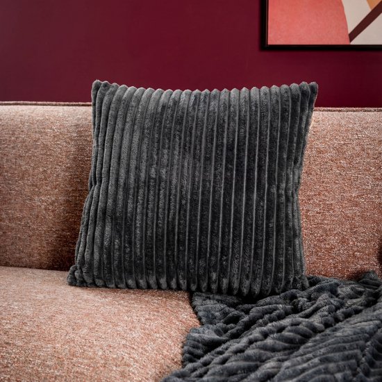 Coussin décoratif gris foncé en velours côtelé sur un canapé rose avec un plaid.