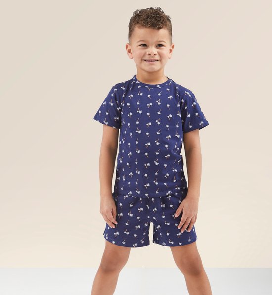 Garçon portant un ensemble pyjama bleu marine à motif de palmiers blancs. T-shirt à manches courtes et short.