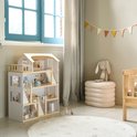 Houten poppenhuis in lichte kleuren, naast een houten ledikant en een ronde witte vloerkleed.