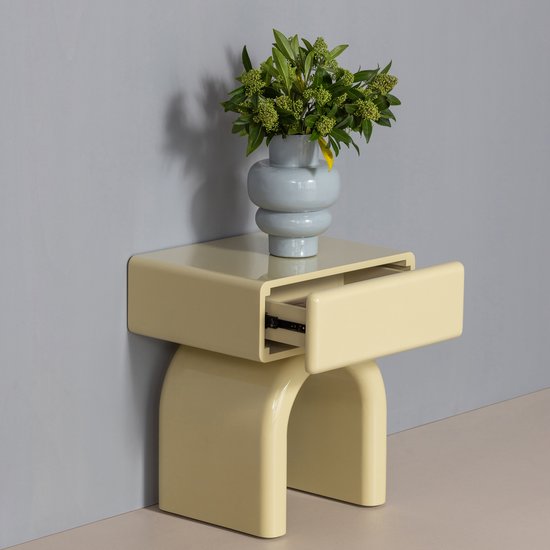 Gele bijzettafel met open lade en een vaas met groene takken erop, tegen een grijze muur.
