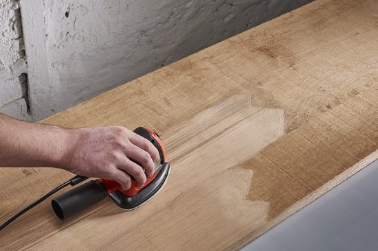 Hand schuurt onbehandeld hout met een schuurmachine, waarbij de houtnerf zichtbaar wordt.