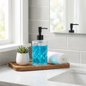 Glazen zeepdispenser met zwarte pomp, gevuld met blauwe zeep, op een houten plankje.