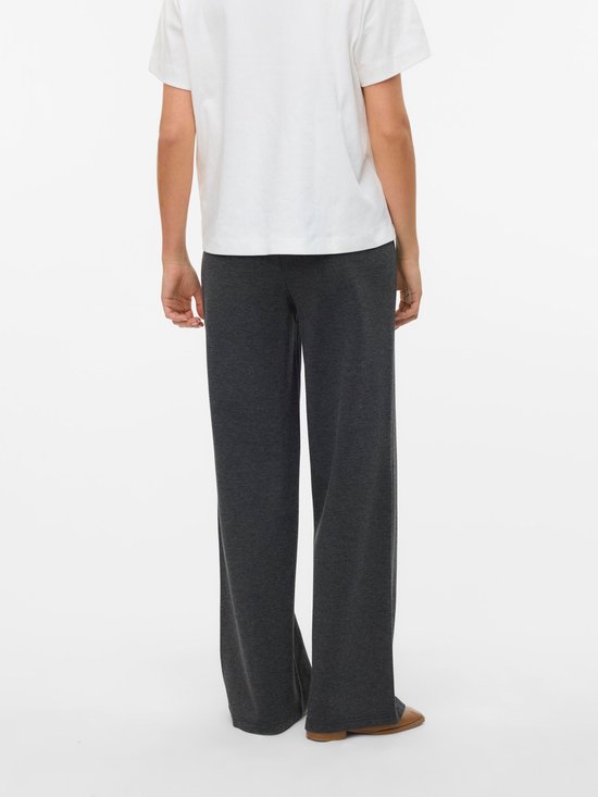 Zijaanzicht van een model in een donkergrijze broek met wijde pijpen en een witte top. De broek heeft een hoge taille.