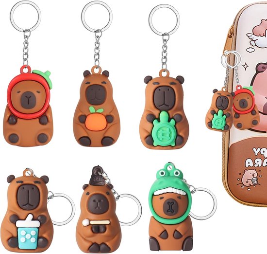 Zeven capybara sleutelhangers: sinaasappel, schildpad, drankje, kikker, hoed, aardbei. Twee van de sleutelhangers zijn bevestigd aan een etui.