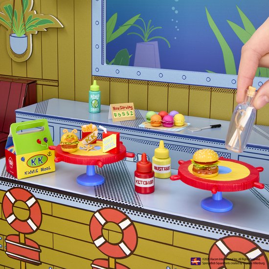 Miniatuur Krabby Patty set met 'Kiddie Meal' lunchbox, ketchup, mosterd, saus en macarons op rode tafels met stuurwiel.